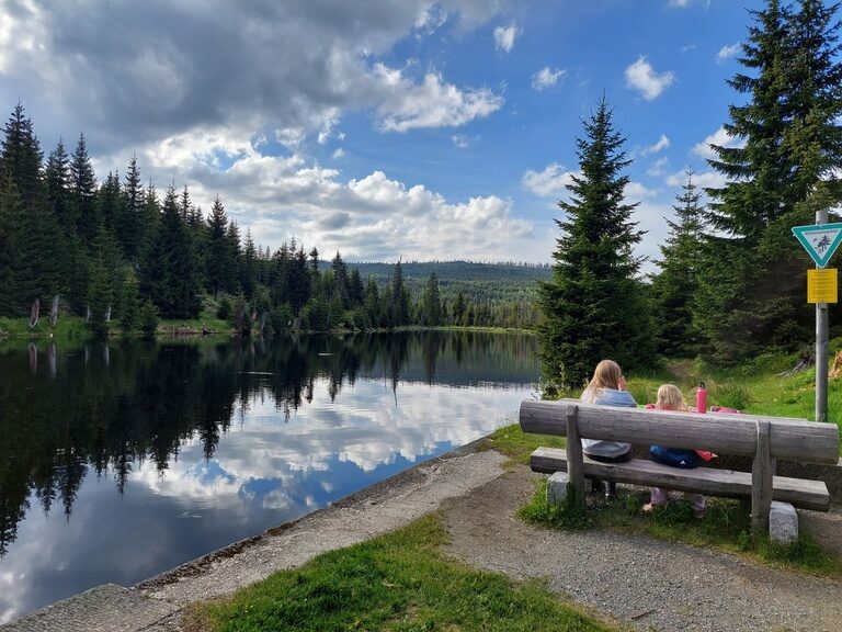 Eine Mutter und Tochter sitzen auf einer Bank im Freien am See und betrachten die grüne Landschaft des Bayerischen Waldes.