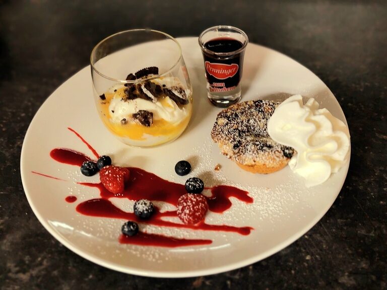 In der Gaststube der Pension Kilger befindet sich auf einem weißen Porzellanteller ein dekorativ gestaltetes Dessert.